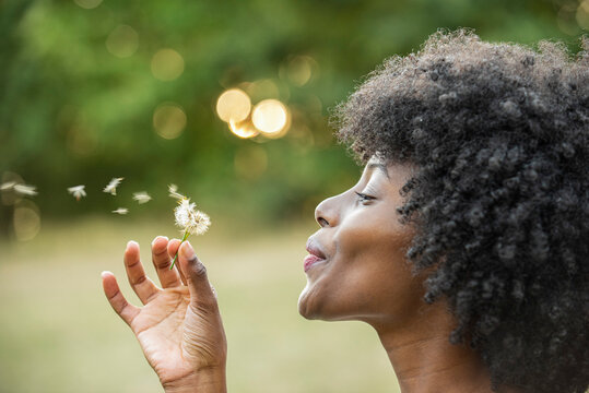 Close-up of young woman blowing dandelion flower