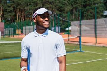 Smiling african american tennis player holding racket on court