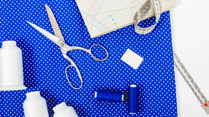 Fashion background. Pattern, blue fabric, threads and various designer accessories on a white table, top view. Space for text