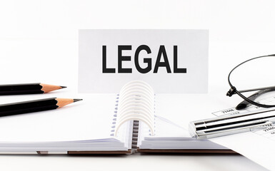 Text LEGAL on paper card,pen, pencils, glasses,financial documentation on the table - business concept