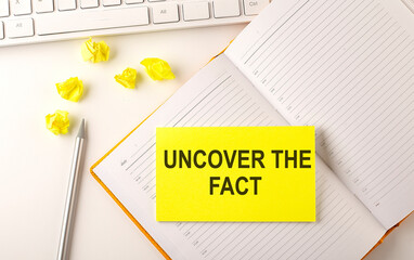 UNCOVER THE FACT text on the sticker on the diary with keyboard and pencil