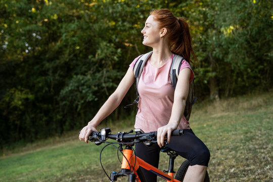 Smiling young woman sitting on bicycle in forest
