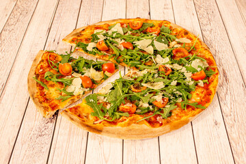 Italian recipe for tri-color pizza with a separate slice. Arugula and parmesan cheese in flakes, pieces of cherry tomatoes and thin wheat flour dough