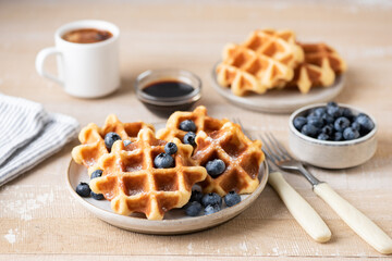 Breakfast belgian waffles with blueberries and cup of coffee on a wooden table. Cafe sweet breakfast served