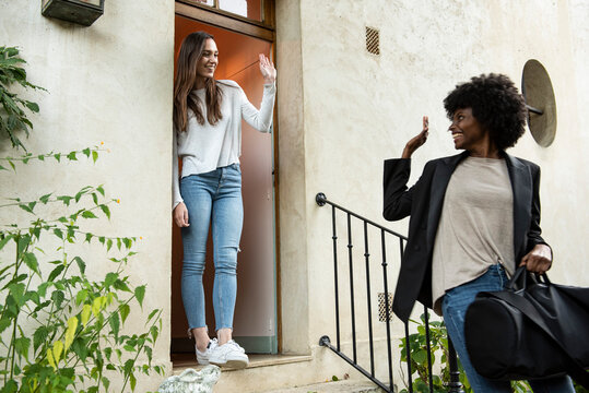 Young Female Friends Waving Hands At Doorstep