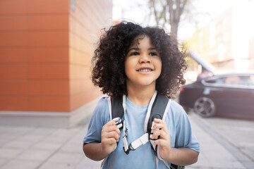 handsome happy boy, afro mixed race, goes on his way to school, with his backpack, starts back to...