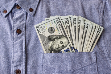 Banknotes of 100 dollars (one hundred) American money pocking out from a pocket of an office style blue color shirt. Paper money, close up