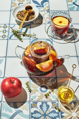 Fruit tea with apples and thyme in glass teapot and cup on table made of colored tiles