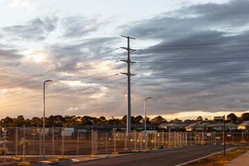Electricity pylon on cloudy sky over road and suburbs.
