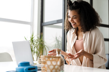 Black young woman smiling and holding copyspace while using laptop