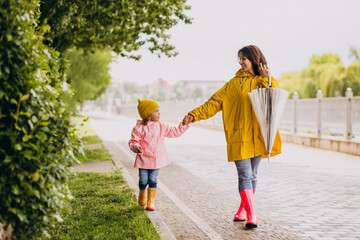Mother with daughter walking in park in the rain wearing rubber boots