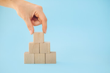 Female hand putting down the wooden cube on top pyramid, for create icon symbol to success and...