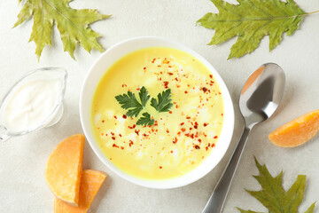 Plate of pumpkin soup and ingredients on white textured table