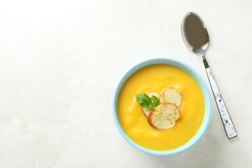 Plate of pumpkin soup and spoon on white textured table