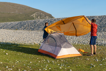 Camping people outdoor lifestyle couple putting up a tent in nature rocky beach.