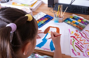 a little girl draws with colored paints, leads with a brush on paper