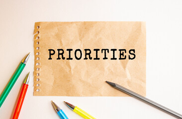 A sheet of kraft paper torn from a notebook lies on the table. Text on PRIORITIES sheet. Colored...