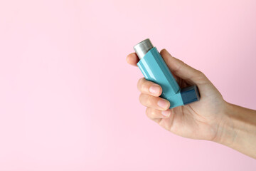 Female hand holds asthma inhaler on pink background - obrazy, fototapety, plakaty