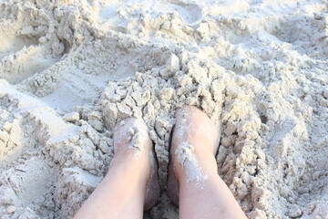 The woman buried her feet in the sand of the sea beach. She is resting. She is calm.