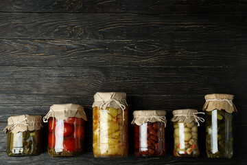 Jars of pickled vegetables on rustic wooden background