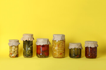 Jars of pickled vegetables on yellow background