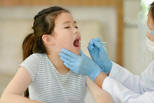 Female pediatrician using a swab to take a sample from a patient's throat.Medical worker taking mucus specimen from potentially infected Asian child. Covid-19 nasal swab test.