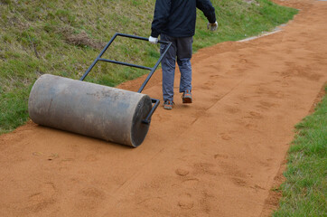 compressing the gravel of the new park threshing path. lawn seed is repaired by rolling a metal...