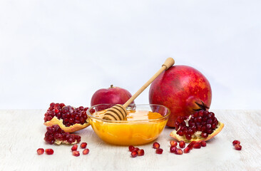 Honey in glass bowl, red apples, garnets, wooden honey dipper on white wooden table on a light background with space for text