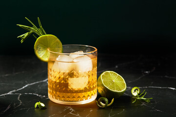 Alcoholic or non-alcoholic cocktail with lime and rosemary on a dark marble table