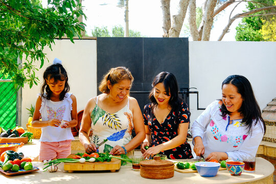 Smiling mature woman preparing salsa with daughters and granddaughter at kitchen counter in backyard during weekend