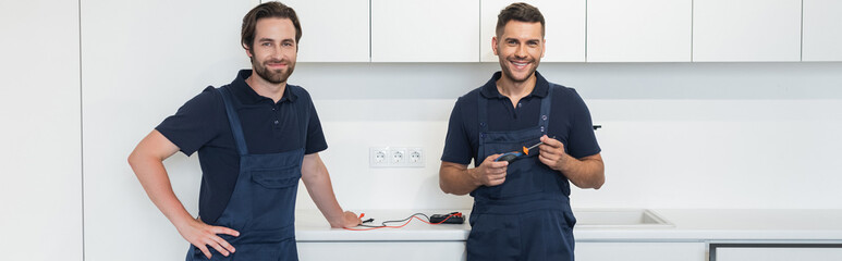 electrician smiling at camera while standing in kitchen, banner