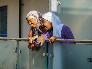 Two young women wearing hijabs leaning on balcony