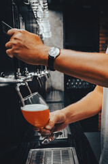 man bartender hand at beer tap pouring a draught beer in glass serving in a restaurant or pub