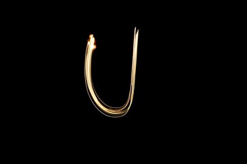 Drawn letter U with gold lights against black background. Light painting alphabet.