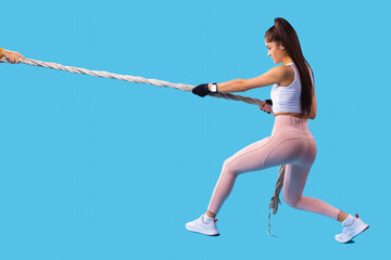 Strong muscled woman posing with the sport rope and making exercises with pulling the rope towards...