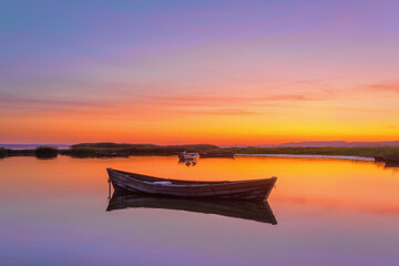 Naklejka premium Lonely wooden boat in calm lake. Amazing sunrise in summer morning. The silhouette is reflecting on the water. Orange sky with clouds. Location place Svityaz lake, Ukraine, Europe.
