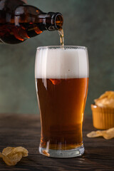 Pouring fresh beer from brown bottle into glass on dark background