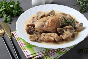 Rabbit meat with mushrooms and sour cream sauce in a white plate on a dark background