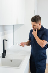 thoughtful handyman holding wrench near sink in kitchen