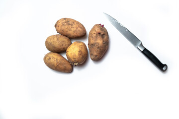 there are potatoes on a white table. next to the knife.