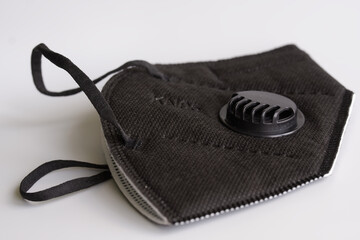 Black respirator with a filter and a valve lies on a white background. The respirator has a KN95 protection class corresponding to the American N95 and European FFP2.