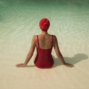 Woman sitting in swimmingpool with red bathing suit and bathcap seen from back in summer