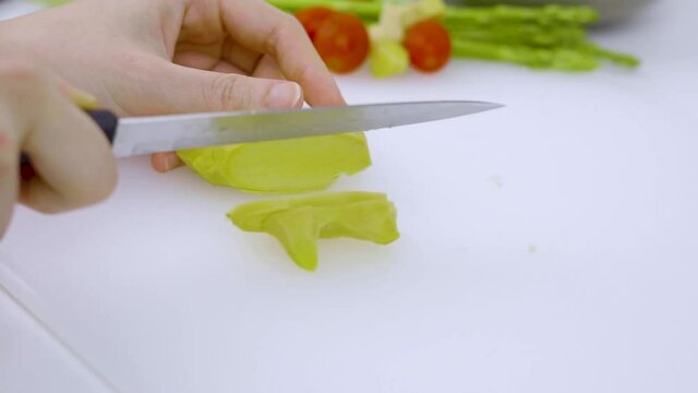 A woman is slicing ginger on a white cutting board.