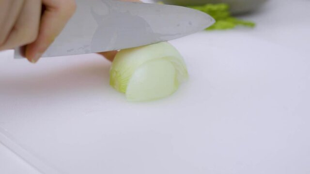 Closeup hands cutting white onion on a white cutting board.
