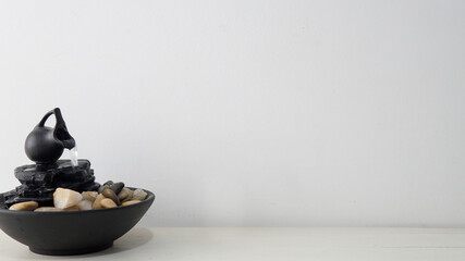   Close view of a zen water fountain over a white wooden table with a white background              