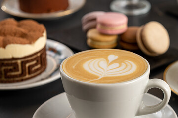 Primer plano de una taza blanca con cafe con diseño de arte latte con macarones de fondo con foco diferenciado