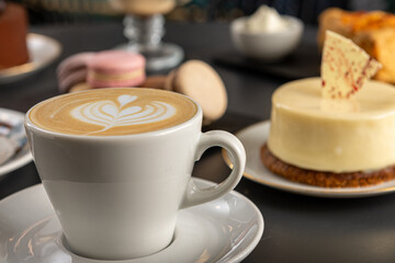 Café  con arte latte en un primer plano acompañado de distintos tipos de tortas con foco...