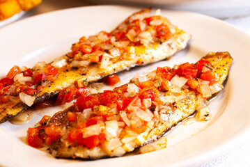 Grilled trout in tomato sauce with onion and pepper. In the background carrot, cabbage and pickle salad