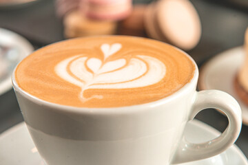 Café  con arte latte en un primer plano acompañado de distintos tipos de tortas con foco diferenciado.