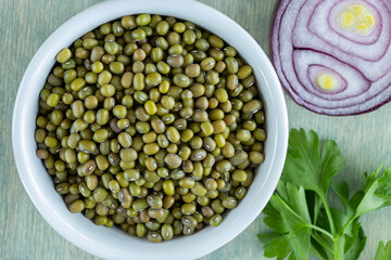 top view on beans of mung sin white plate with onion and parsley. close up mung on a green wooden background. Flat lay.